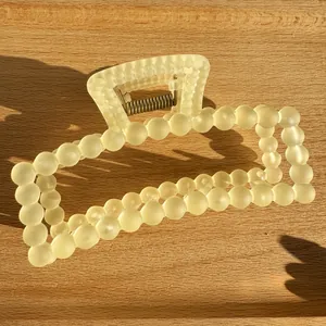 Detail of matte cream yellow square hair claw clip on light wood texture surface
