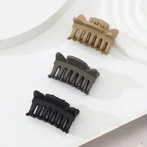 Three matte hair clips in beige, grey, and black on minimalist geometric display stands