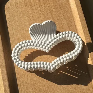 Detail of white heart-shaped matte hair claw clip with beaded edges on a wooden tray