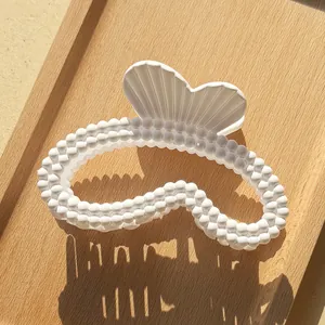 Dettaglio di una pinza per capelli bianca con texture a perle su un vassoio di legno ed ombre
