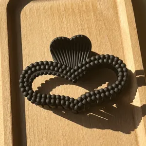 Macro view of a black heart-shaped hair claw clip with a beaded texture on wooden tray