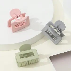 Detailed view of three matte small hair claws in pink, grey, and green on a white pedestal