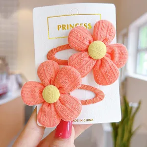 Detailed view of two handmade knitted coral pink flower hair clips for girls on display card