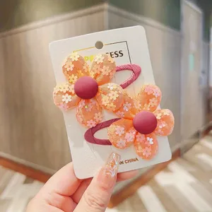 Detail of two orange mesh flower hair clips for girls on a white card board