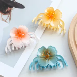Three gradient floral hair claws in pink, yellow, and blue on a stylish wooden tray