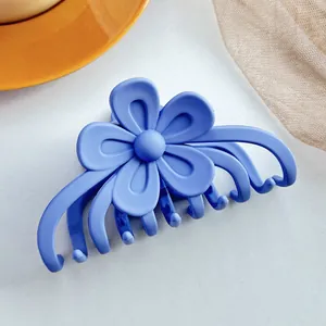 Détail d'une pince à cheveux fleur bleue mate avec dents imbriquées sur fond gris