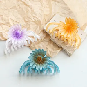 Drei bunte Gänseblümchen-Haarklammern in Lila, Gelb und Blau auf einem Marmorsockel