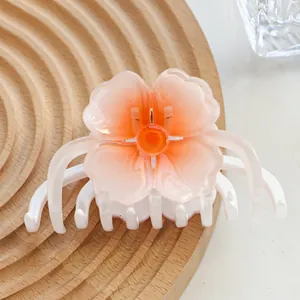 Macro shot of gradient orange resin flower hair claw clip on a textured wooden tray