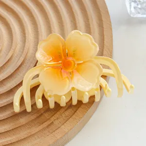 Close-up of a gradient yellow frangipani hair claw clip on a textured wooden tray