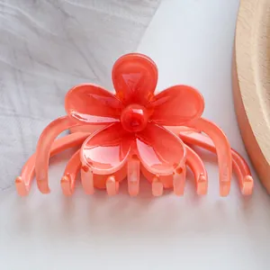 Detail shot of a coral orange glossy flower hair claw clip on a wooden display tray