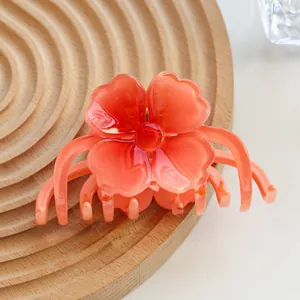 Close-up of translucent orange plumeria hair claw on a minimalist wooden tray