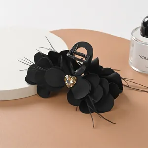 Dettaglio del fermaglio nero con petali di tessuto, piume e un cristallo a cuore