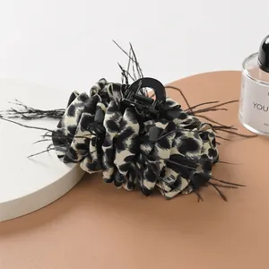 Detail of leopard print fabric hair claw clip with elegant black feathers and resin base