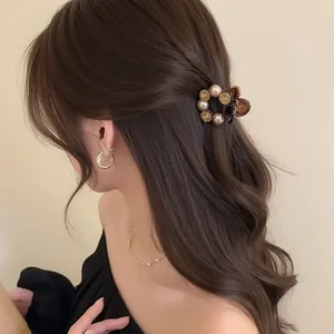Eleganter Perlen-Haarclip mit goldenen Blumenakzenten auf lockigem Haar