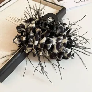 Detail view of large leopard print hair claw with feathers and ruffled fabric textures