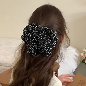 Detailed view of a retro triple-layered black polka dot bow clip on wavy hair