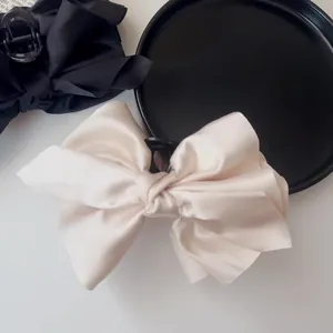 Macro detail of silk-satin bow hair claws in cream and black with smooth fabric texture