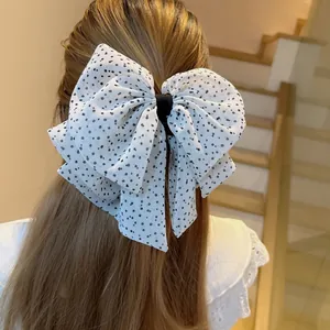 Detail of white chiffon three-layer polka dot bow hair clip shown on the back of the head