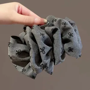 Close-up of large hair claw clip with black bow pattern on pleated fabric texture