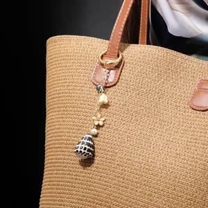 Close-up of ocean shell keychain with pearl and metal flower on a straw bag