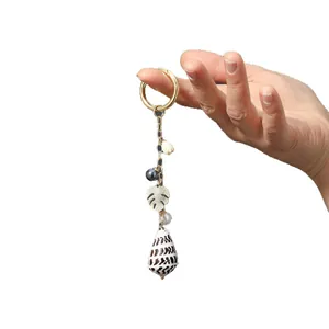 Golden keychain with natural cone shell, Monstera leaf charm, and pearl on white background