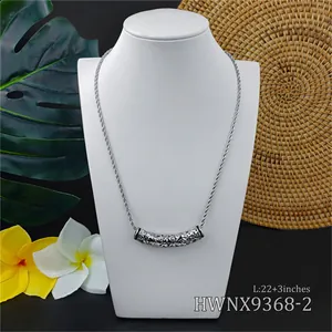 Engraved Hawaiian cylinder pendant necklace on model with monstera leaf background