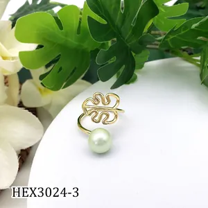 Detail van gouden monstera blad ring met groene parel op witte standaard