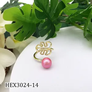 Detail van een gouden monstera blad ring met roze parel op een witte sokkel