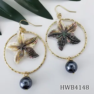 Détail de créoles dorées avec pendentifs étoile de mer en nacre et perles grises