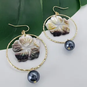 Créoles dorées avec fleur en coquillage et perle foncée sur fond de feuilles vertes