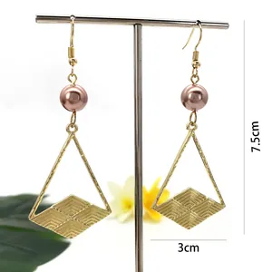 Dettaglio di orecchini geometrici lunghi 7,5cm con perla rosa e motivo a rombo inciso