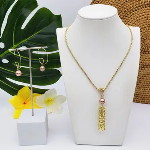 Détail du collier à tube doré et boucles d'oreilles créoles avec perles roses sur fond tropical