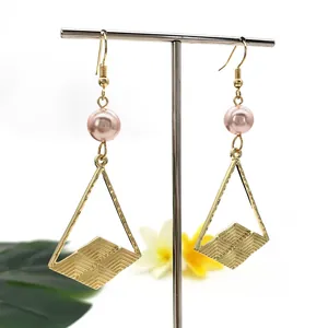 Dettaglio di orecchini geometrici con cornici a triangolo dorato e perle rosa su supporto