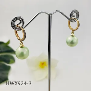 Dettaglio di orecchini huggie dorati con zirconi cubici e perle di colore verde chiaro