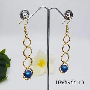 Detailansicht langer goldener Ohrringe mit Hammerschlag-Ringen und blauer Perle