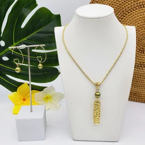 Détail du collier doré et des boucles d'oreilles avec perles vertes et motifs tropicaux