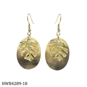 Macro shot of gold Monstera leaf earrings on oval mother of pearl shell with hook