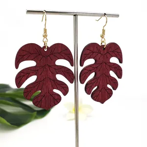 Donkerrode monstera blad houten oorbellen met gouden haken op witte standaard