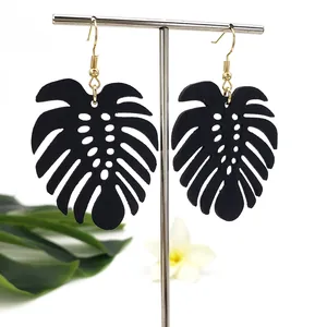 Detail van zwarte monstera oorbellen met gouden haakjes op tropische displaystandaard