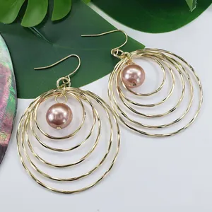 Layered gold hoop earrings featuring five concentric circles and a pink pearl drop charm