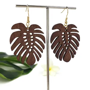 Detail van donkerbruine houten monstera blad oorbellen met gouden haken op standaard
