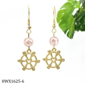Detail von langen goldenen Ohrhängern mit rosa Perle und einem goldenen Steuerrad-Anhänger
