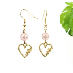 Detail goldene Herzohrringe mit Love Gravur und einer rosa Perle als Akzent