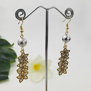 Détail de boucles d'oreilles pendantes fleurs dorées avec perle sur un support en T