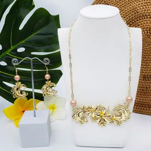 Détail de la parure de bijoux fleurs dorées avec perles roses sur feuilles tropicales