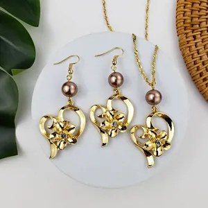 Dettaglio di un set di gioielli cuore dorato e fiore con perle su base in marmo