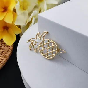 Détail d'une pince à cheveux ananas évidée en métal doré sur un socle blanc