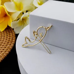 Détail d'une barrette en métal doré avec motif dauphin ajouré et finition polie
