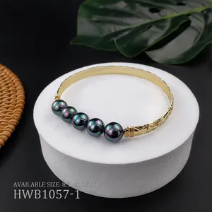 Dettaglio del bracciale dorato inciso con perle di conchiglia nere e base tropicale