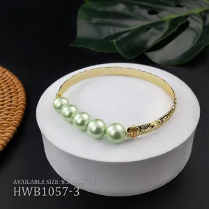 Bracciale rigido dorato inciso con cinque perle verde chiaro su espositore bianco